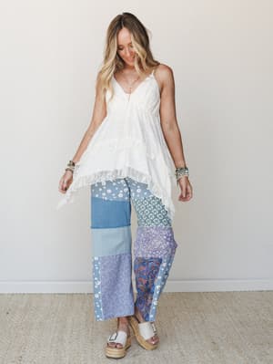 A flowy white lace-trim cami top paired with wide-leg patchwork pants in mixed blue prints — daisy, paisley, bandana, and denim — styled with platform espadrille sandals and stacked bracelets for a free-spirited, collected look.