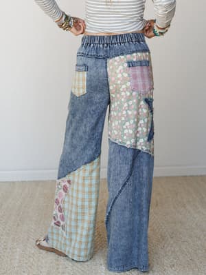 A back-view shot of wide-leg patchwork denim pants styled with a striped crop top and stacked bracelets — the kind of pants that make a whole outfit out of themselves.