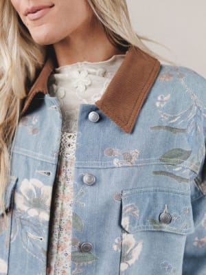 Close-up of a person wearing a floral dress under a denim jacket with brown collar.