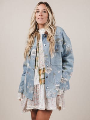Woman wearing a floral dress under a denim jacket on a plain background