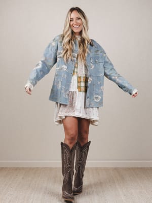 Woman wearing a floral dress, denim jacket, and cowboy boots against a plain background