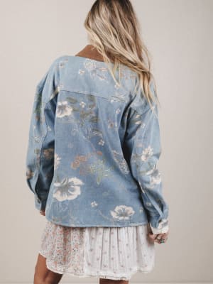 Person wearing a floral denim jacket over a white dress on a plain background