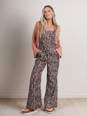 Woman wearing a floral jumpsuit with a pink cardigan against a plain background