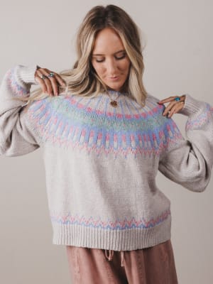 Woman wearing a gray sweater with colorful pattern on a plain background