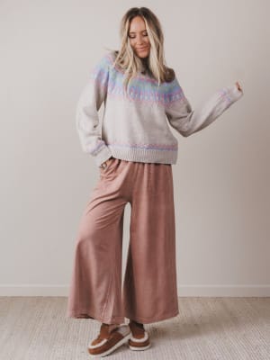 Woman wearing a patterned sweater and wide-leg pants against a plain background