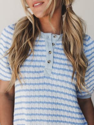 A close-up of a textured stripe henley top in soft periwinkle and cream — the kind of easy, feel-good piece that looks just as good for a slow morning in as it does running errands.