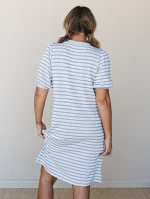 A back-view shot of a textured stripe mini dress in soft periwinkle and cream — easy, lived-in, the kind of thing you'd wear all day and not want to take off.