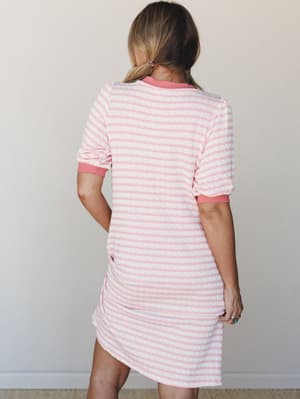 A back view of a textured stripe knit mini dress in pink and white, styled simply against a neutral wall — the kind of piece that blurs the line between getting cozy and going somewhere.