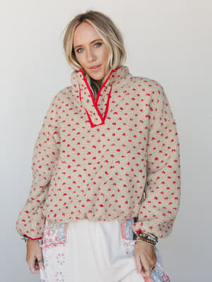 A cozy sherpa pullover in oatmeal with red speckled texture and contrast red trim at the collar, layered over a mixed floral print skirt with stacked boho bracelets — the kind of outfit that makes a Saturday morning feel intentional.