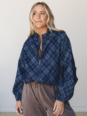 A relaxed cropped plaid jacket in deep navy worn half-open over a muted brown top and wide-leg pants — the kind of effortless layering that makes a Tuesday feel intentional.
