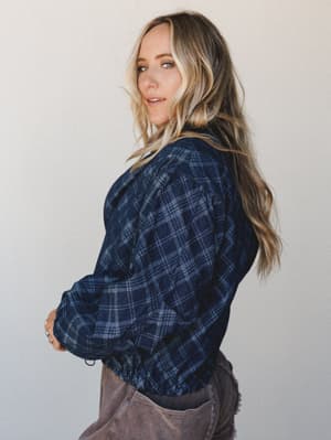 A model looks back over her shoulder in a roomy navy plaid jacket paired with washed charcoal jeans — the kind of effortless layer that makes a Saturday errand feel intentional.