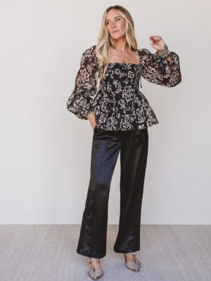 Woman wearing a floral blouse and black pants against a white background