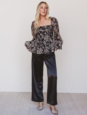 Woman wearing a black floral top and black pants against a white background