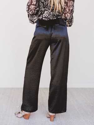 Person wearing black satin pants with a patterned top against a white background