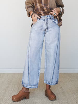 Wide-leg light wash jeans styled with a plaid flannel shirt and wood-studded clogs — the kind of effortless, lived-in combo that looks like it came together without trying but absolutely didn't.