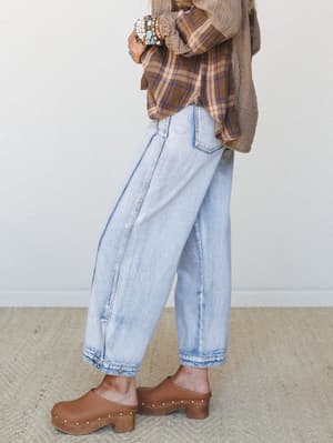 A side-profile shot of wide-leg light wash jeans styled with an oversized plaid shirt, stacked turquoise bracelets, and studded brown clogs — the kind of effortless, lived-in look that feels equally at home on a coffee run or a farmers market morning
