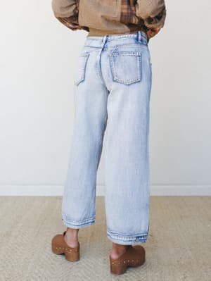 A back-view shot of wide-leg light wash jeans styled with a plaid top and wood-studded clogs — the kind of easy, lived-in denim that feels as good as it looks.