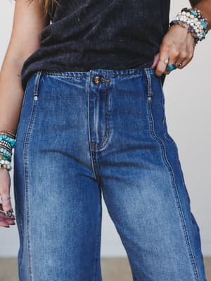 A close-up waist shot of medium wash wide-leg jeans styled with a washed black tee and an arm stacked with turquoise and beaded bracelets — the kind of effortless denim look that pulls itself together without trying.