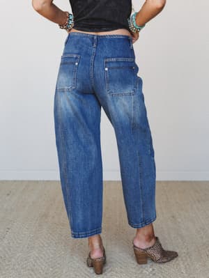 A back-view shot of relaxed barrel-leg jeans in medium denim, styled with a black cropped tee, leopard print mules, and stacked turquoise bracelets — the kind of effortless combo that looks like it took five minutes and somehow works perfectly.
