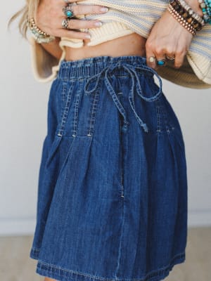 A close-up of a relaxed denim mini skort with a drawstring elastic waist, styled with a cropped striped knit and layered silver and turquoise jewelry — casual and collected with a effortless boho ease.
