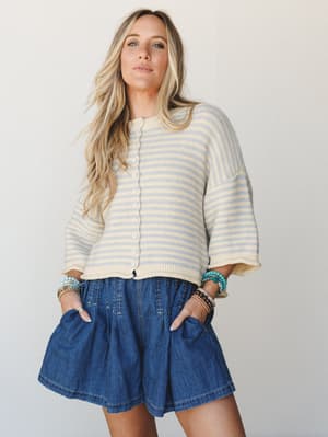 A cropped striped knit cardigan paired with flowy denim shorts and stacked beaded bracelets — the kind of effortless warm-weather outfit that looks like you tried just the right amount.