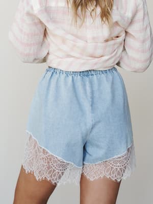 Light wash denim shorts with a sweeping lace hem trim, styled with a knotted pink plaid top — soft, feminine, and just a little unexpected.