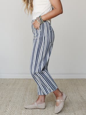 A side-profile shot of striped wide-leg pants in navy and cream paired with a white tee, woven flats, and a stack of turquoise bracelets — the kind of outfit that makes a farmers market feel like a coastal vacation.
