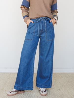 Wide-leg denim jeans with a drawstring waist and patch pockets, styled with a layered mixed-print top and leopard sneakers for an easy, expressive everyday look.