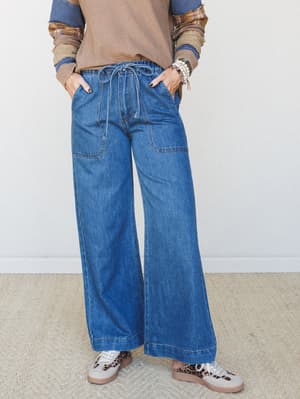 Wide-leg denim jeans with a relaxed drawstring waist, styled with a layered mixed-print top and leopard sneakers — the kind of outfit that looks intentional without trying too hard.