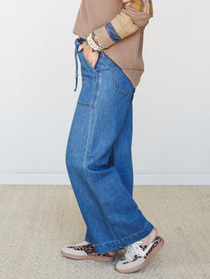 A side-profile shot of wide-leg medium-wash jeans styled with a mixed-fabric sweatshirt, leopard print sneakers, and stacked bead bracelets — the kind of put-together casual that looks effortless but absolutely isn't.