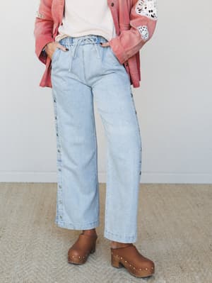Light-wash wide-leg jeans with side snap buttons and a drawstring waist, styled with a dusty rose jacket featuring crochet sleeve trim and paired with wood-studded clogs — the kind of effortless, lived-in outfit that looks like it came together on pu