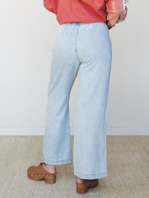 A back-view shot of wide-leg light wash denim pants styled with a coral top and brown wood-platform clogs — relaxed, lived-in, and very much the kind of outfit that makes errands feel intentional.