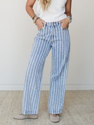 Wide-leg light denim jeans in a pinstripe wash styled with a white knit top, woven flats, and stacked boho jewelry — the kind of outfit that does the heavy lifting without trying too hard.