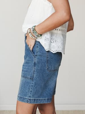 A side-angle close-up of an eyelet crop top tucked loosely over medium-wash denim shorts, styled with a stack of beaded bracelets — casual and collected, the kind of outfit you reach for without thinking twice.