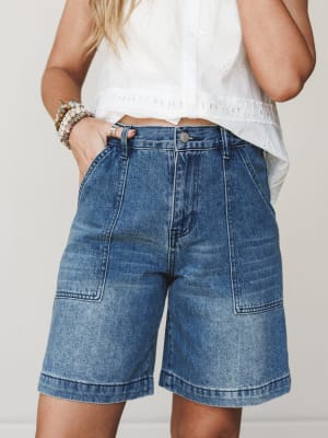 A cropped mid-shot of relaxed, longer-length denim shorts paired with a white eyelet top — the kind of effortless summer outfit that goes from the farmers market straight to lunch.