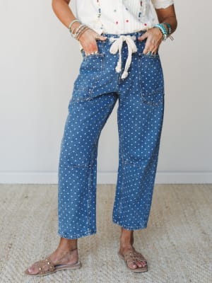 Polka dot wide-leg denim jeans with a rope tie waist and utility patch pockets, styled with an embroidered white top, stacked bracelets, and studded sandals — the kind of outfit that looks effortless but very much on purpose.