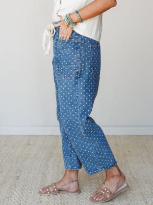 A side-profile shot of polka dot denim jeans styled with a cream tie-front top, turquoise bead bracelets, and studded sandals — playful and relaxed with a distinctly boho-casual feel.