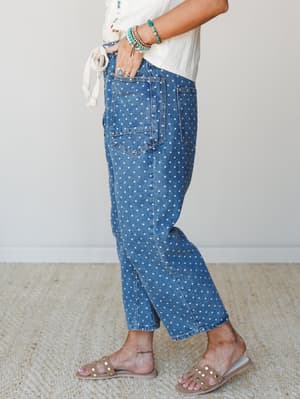 A side-profile shot of polka dot denim jeans styled with a cream tie-front top, turquoise bead bracelets, and studded sandals — playful and relaxed with a distinctly boho-casual feel.