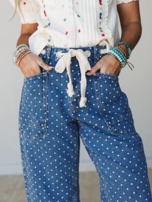 A close-up of polka dot wide-leg jeans with a rope drawstring waist, styled with an embroidered cream top and stacked beaded bracelets — the kind of outfit that feels effortless but clearly thought through.