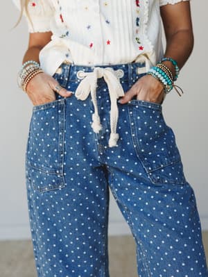A close-up of polka dot wide-leg jeans with a rope drawstring waist, styled with an embroidered cream top and stacked beaded bracelets — the kind of outfit that feels effortless but clearly thought through.