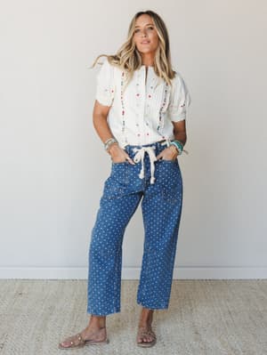 A breezy, expressive full-body shot of a model in polka dot wide-leg denim paired with a cream embroidered blouse — the kind of outfit that feels intentional without trying too hard.