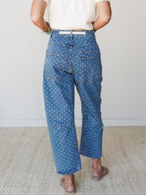 Shot from behind, a model wears wide-leg polka dot denim jeans paired with a cropped cream top and tan sandals — the kind of outfit that feels vintage-y and playful without trying too hard.