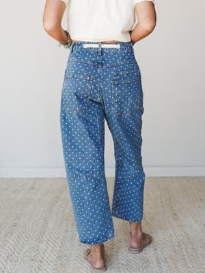 Shot from behind, a model wears wide-leg polka dot denim jeans paired with a cropped cream top and tan sandals — the kind of outfit that feels vintage-y and playful without trying too hard.