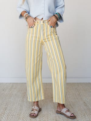 Yellow multi-stripe barrel pants styled with a powder blue knit cardigan, layered beaded bracelets, and buckle sandals — easy, warm-weather dressing with a vintage-leaning, color-happy personality.