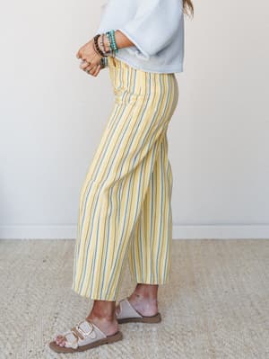 A side-profile shot of wide-leg cropped pants in a sunny yellow stripe, styled with a soft blue knit crop and stacked beaded bracelets — the kind of outfit that feels like a farmers market Saturday with nowhere to be.