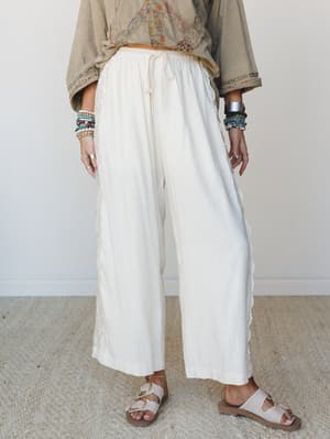 Breezy ivory wide-leg pants with lace side trim and a drawstring waist, styled with a boho floral top, stacked bracelets, and buckle sandals — the kind of outfit that looks effortless but was absolutely thought about.