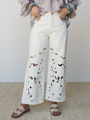Cream wide-leg jeans with allover eyelet cutout detailing styled with a flowy paisley top, stacked bead bracelets, and neutral buckle sandals — the kind of outfit that looks effortless but definitely took a second.