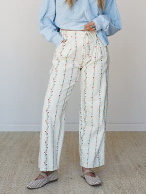 Wide-leg cream pants covered in vertical embroidered floral vine stripes, styled with a powder blue cropped sweatshirt and woven flats — the kind of outfit that looks intentional without trying too hard.