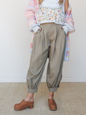 A relaxed, earthy outfit built around olive barrel-leg pants with elasticated cuffs, layered under a floral crop top and a soft multicolor knit cardigan, finished with studded wood clogs — the kind of outfit that feels intentional without trying too
