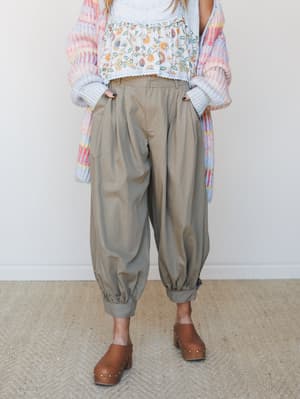A relaxed, layered outfit built around olive barrel pants with elasticated cuffs, styled with a floral crop top, pastel multicolor knit cardigan, and brown studded clogs — the kind of put-together-but-effortless look that feels intentional without tr